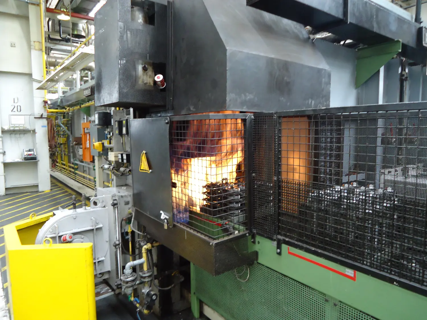 Eine Industriemaschine, möglicherweise ein Ofen oder eine Wärmebehandlungsanlage, angesichts der sichtbaren Flammen und der industriellen Umgebung.