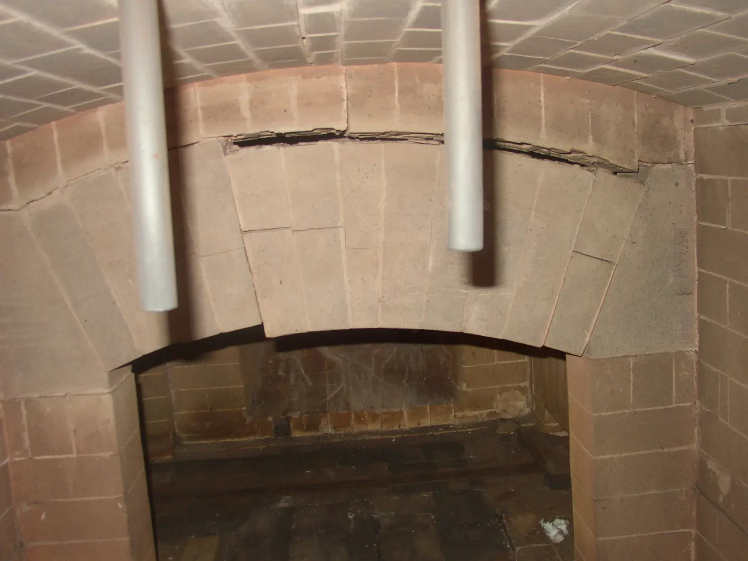 das Innere eines gemauerten Gebäudes, wahrscheinlich eines Holzofens oder Kamins, mit besonderem Augenmerk auf die gewölbte Öffnung des Feuerraums oder Garraums. Von Härterei Service Dirk Gieselmann